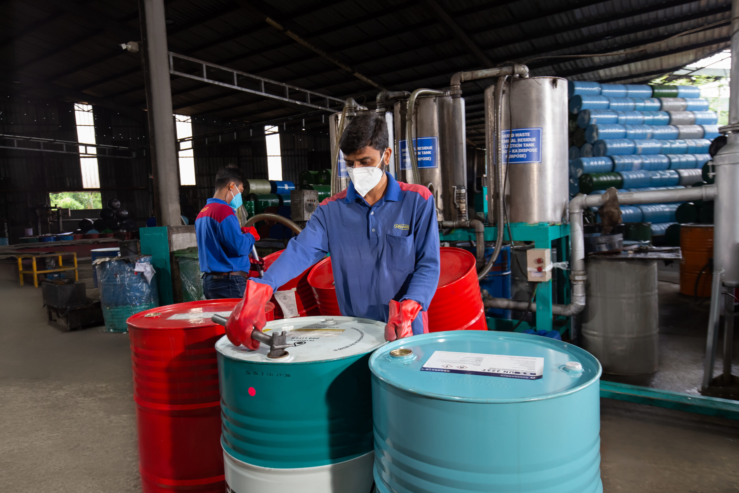 Workers handling metal drums inside an industrial facility
