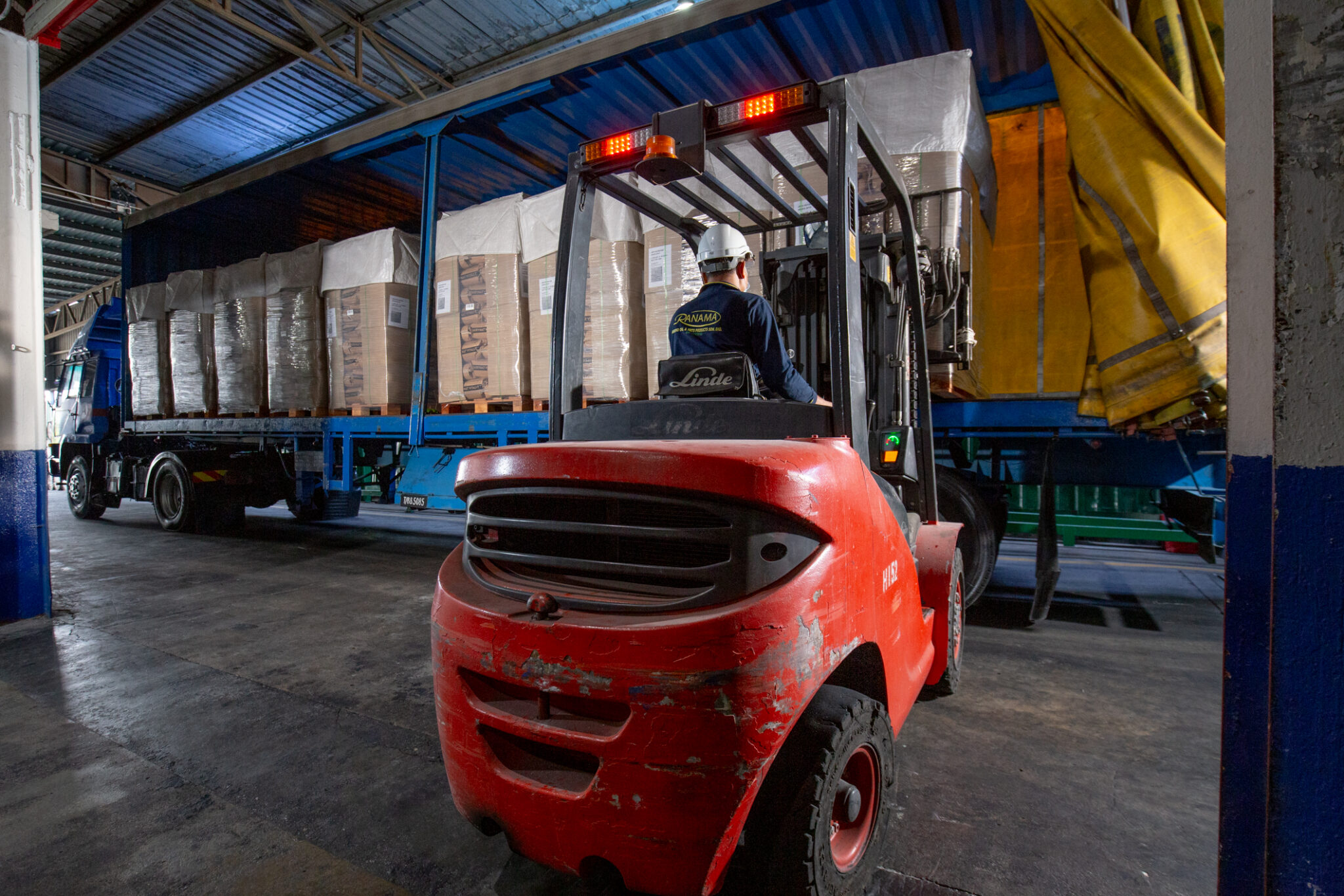 Forklift handling rows of wrapped palletised materials beside an industrial transport vehicle